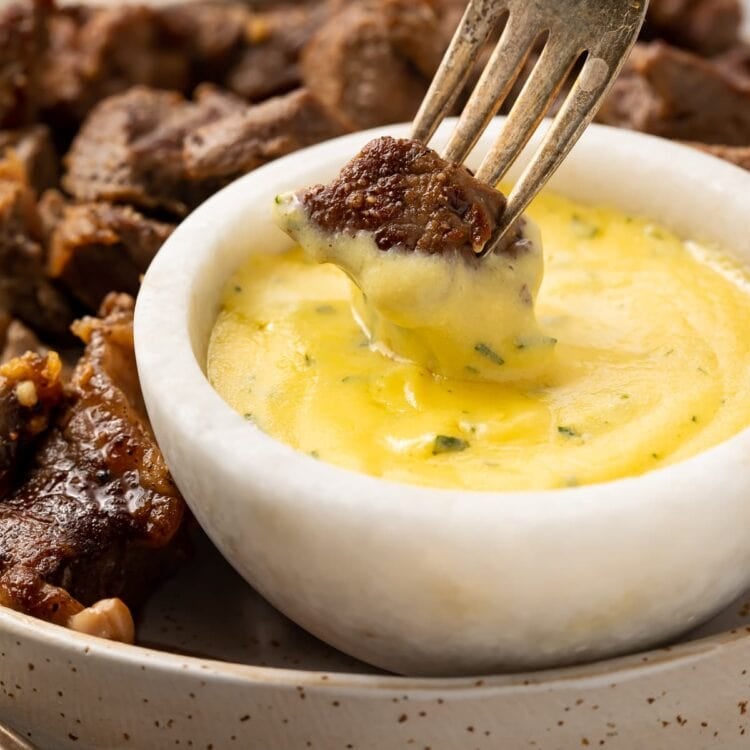 Garlic steak bite on the end of a fork, being dipped into a small bowl of microwave bearnaise sauce