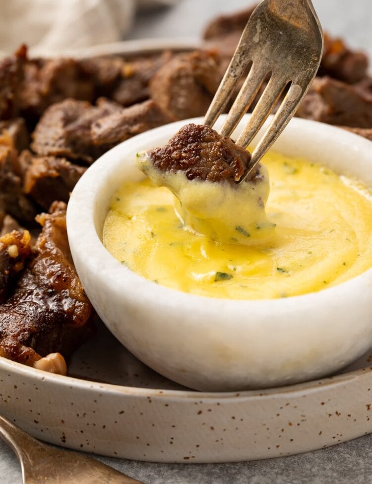 Garlic steak bite on the end of a fork, being dipped into a small bowl of microwave bearnaise sauce
