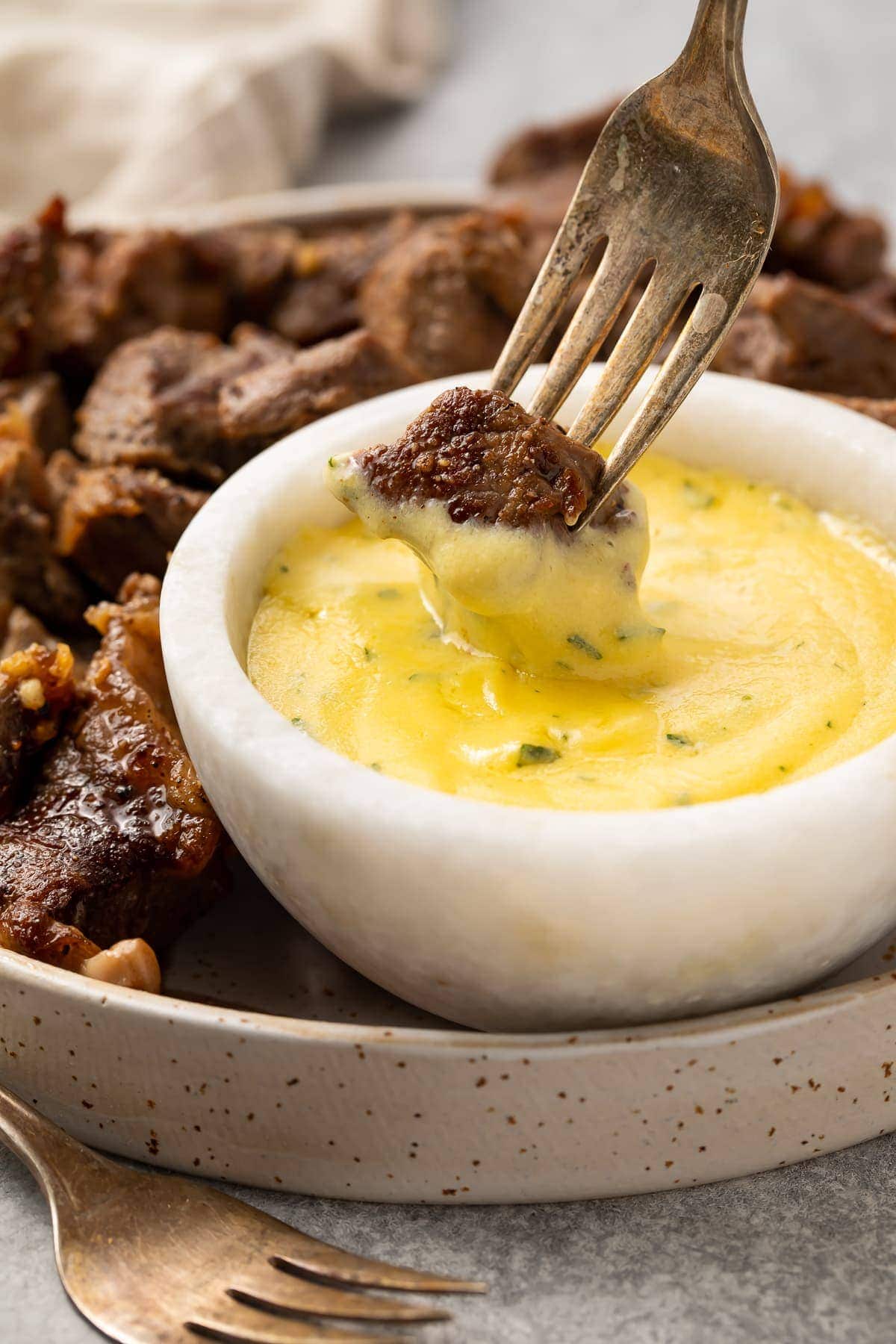 Garlic steak bite on the end of a fork, being dipped into a small bowl of microwave bearnaise sauce