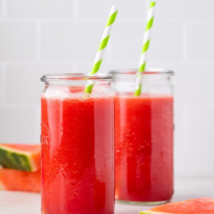 Zoomed out photo of two glasses of watermelon juice in front of slices of watermelon