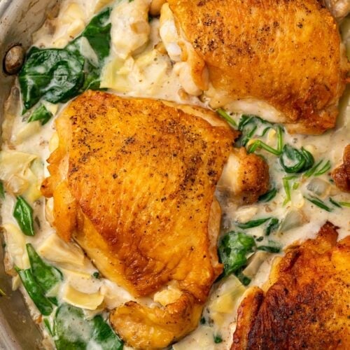 Close up photo of paleo spinach and artichoke chicken in a large silver pan. Chicken is uncovered by spinach artichoke sauce