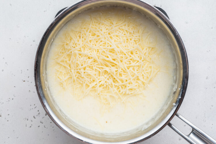 Overhead view of grits and cream in a heavy saucepan with fresh shredded cheese.