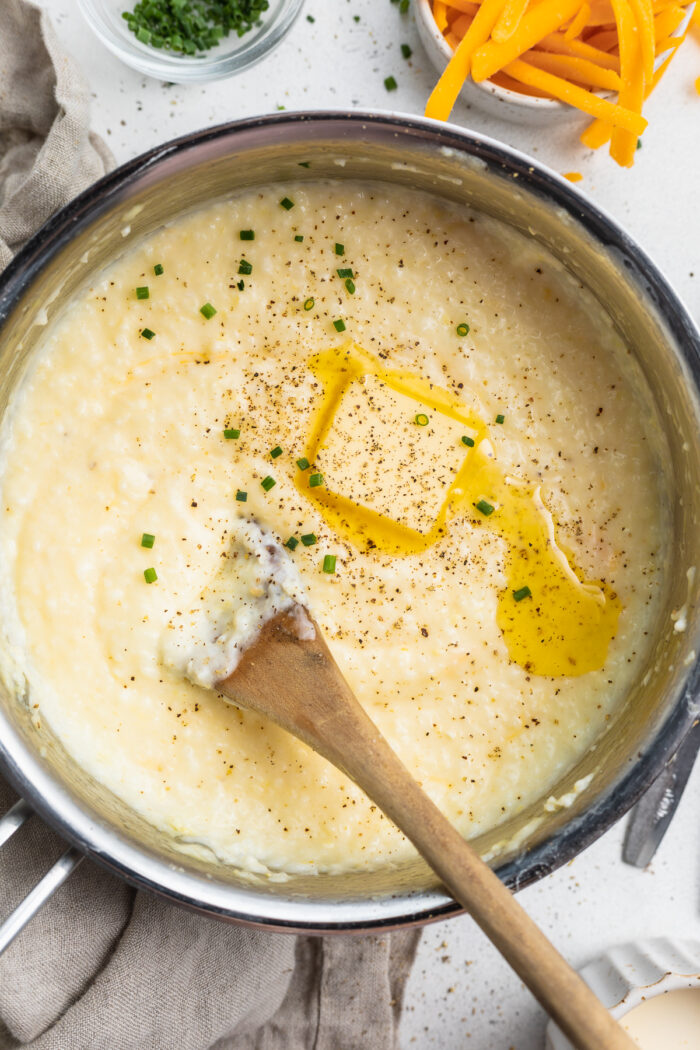 Overhead view of creamy grits in a large silver saucepan with cheese and black pepper.