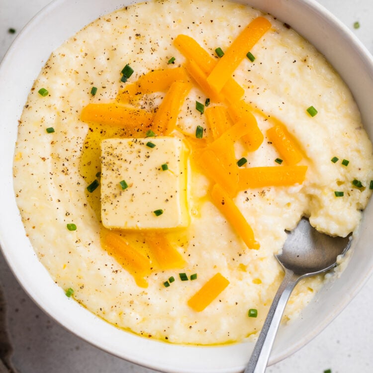 Overhead view of a white bowl of grits topped with shredded cheese, a pat of butter, and black pepper.