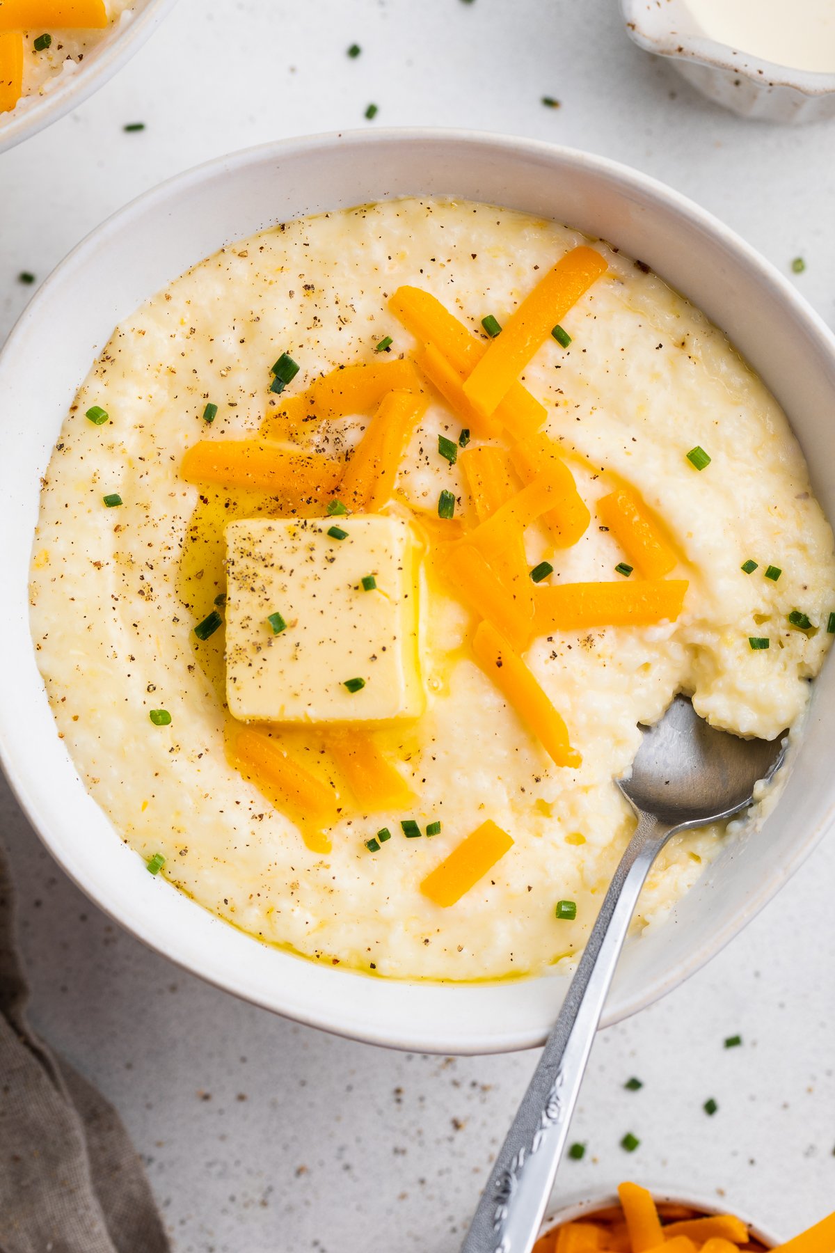 Overhead view of a white bowl of grits topped with shredded cheese, a pat of butter, and black pepper.
