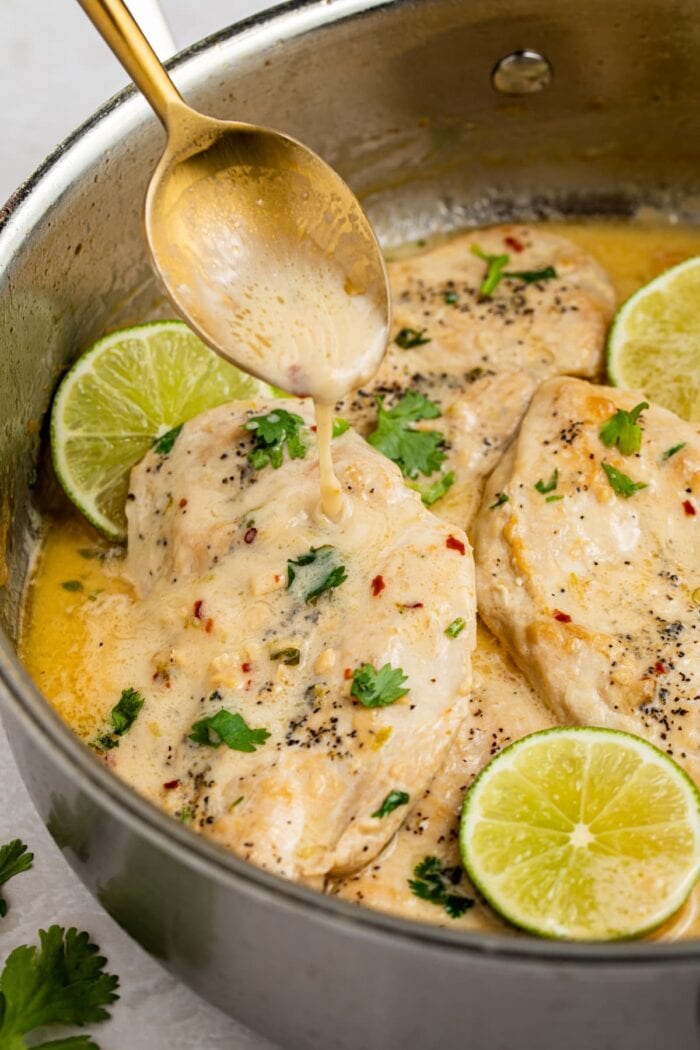 sauce being spooned over coconut chicken in a skillet