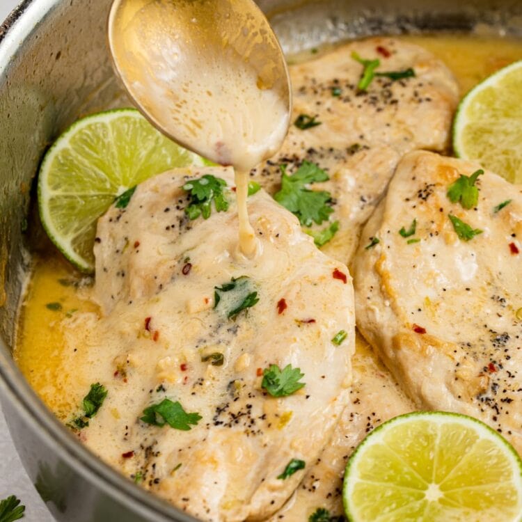 sauce being spooned over coconut chicken in a skillet