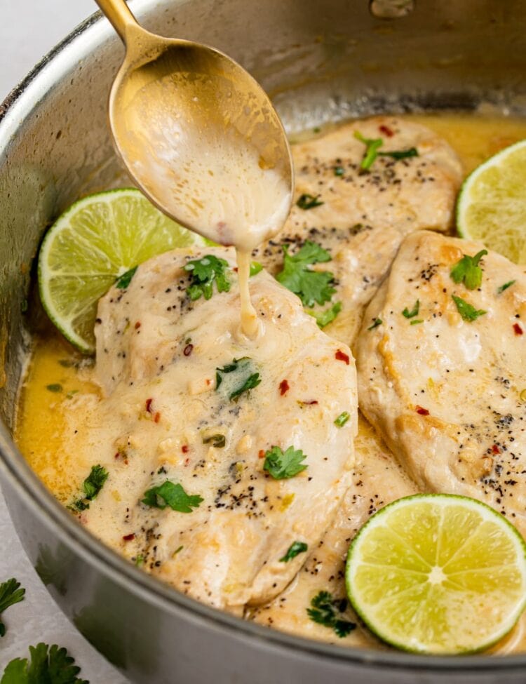 sauce being spooned over coconut chicken in a skillet