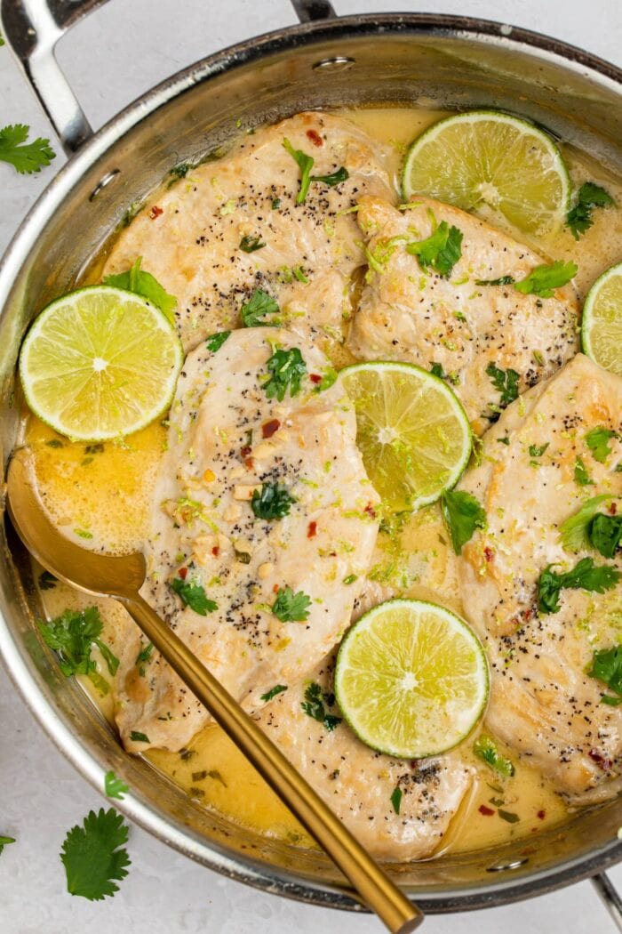 coconut chicken in a skillet with lime slices and cilantro