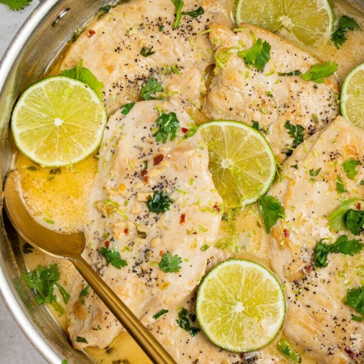 coconut chicken in a skillet with lime slices and cilantro