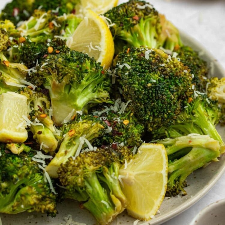 grilled broccoli on a plate with lemon slices and parmesan cheese on the side