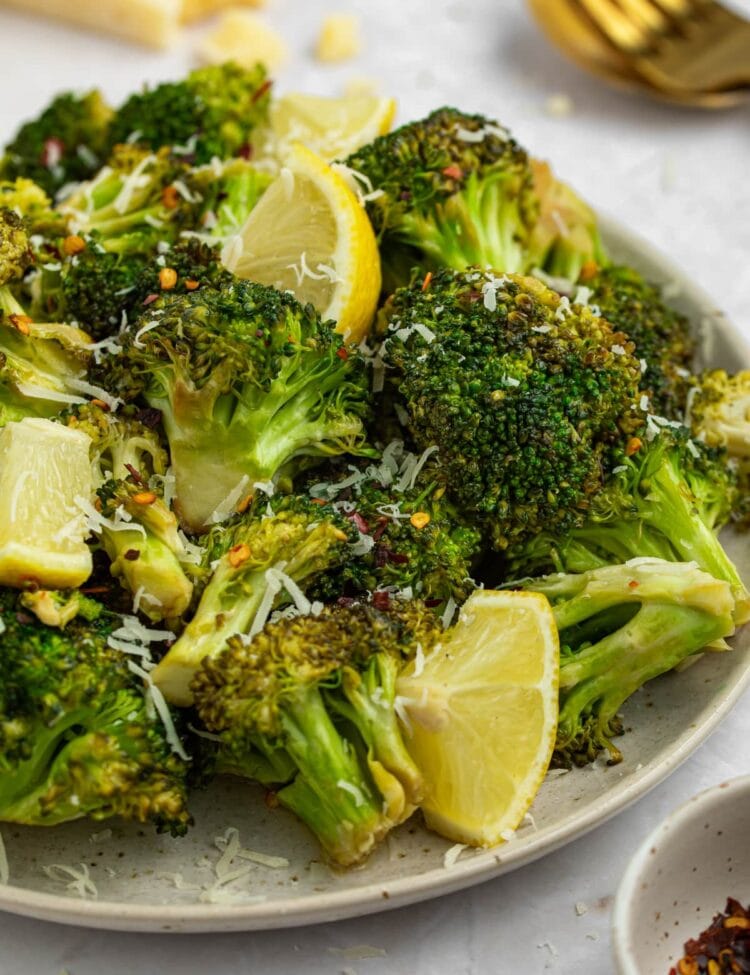 grilled broccoli on a plate with lemon slices and parmesan cheese on the side