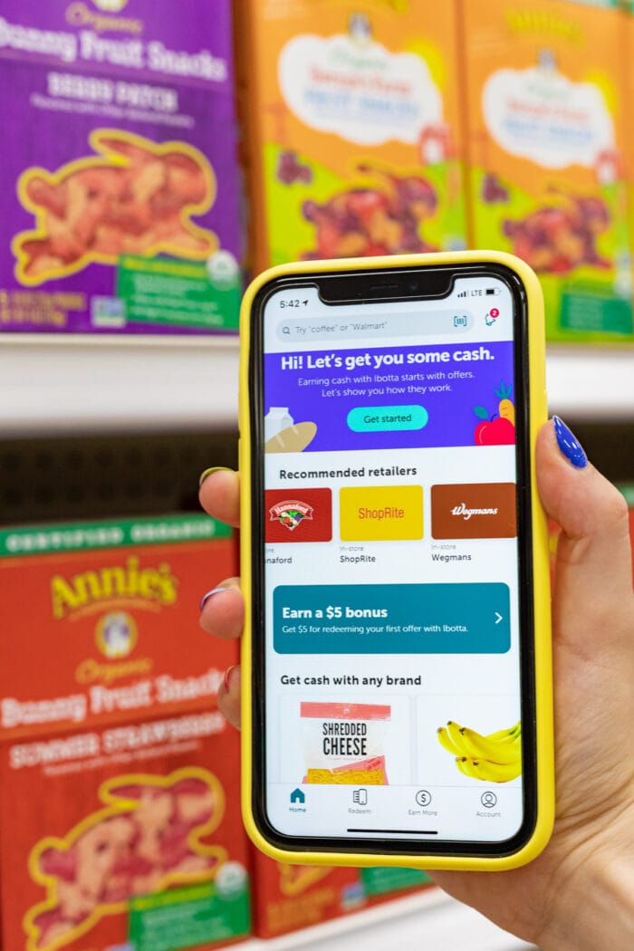 Ibotta app on iPhone in yellow case in front of a row of healthy snacks in a grocery store