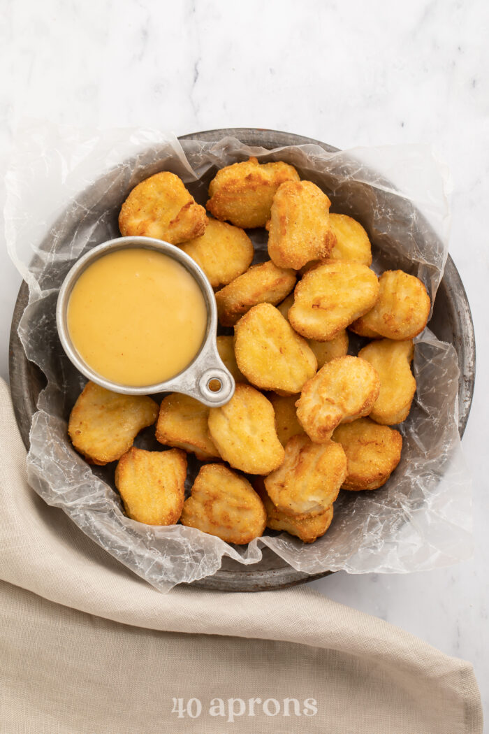 Overhead view of a large bowl of air fryer frozen chicken nuggets with a small dipping bowl of honey mustard.
