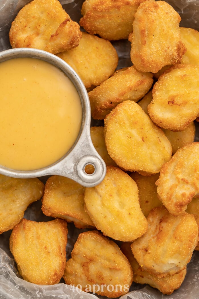 Close-up of air fryer frozen chicken nuggets in a large bowl, next to a small dipping bowl filled with honey mustard sauce.