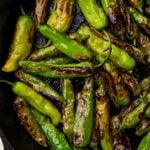 Blistered shishito peppers in a large cast iron skillet