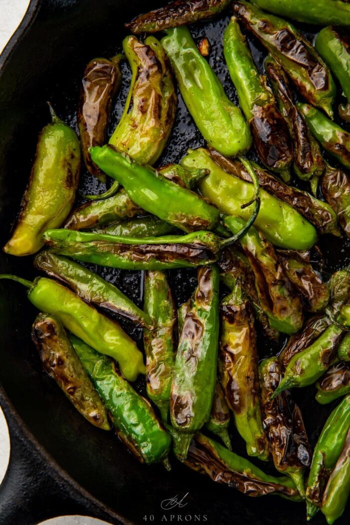 Blistered shishito peppers in a large cast iron skillet