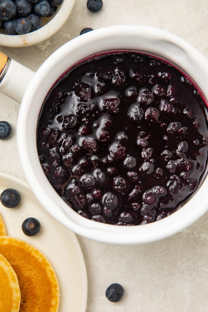 Overhead view of a white bowl of blueberry compote on a light countertop