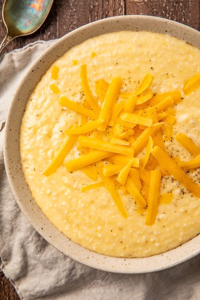 Cheese grits in a tan bowl with shredded cheese on top