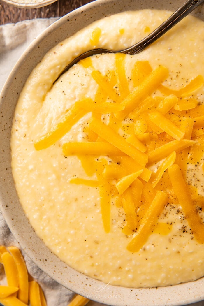 Close up of cheese grits in a stone bowl, with shredded cheese on top