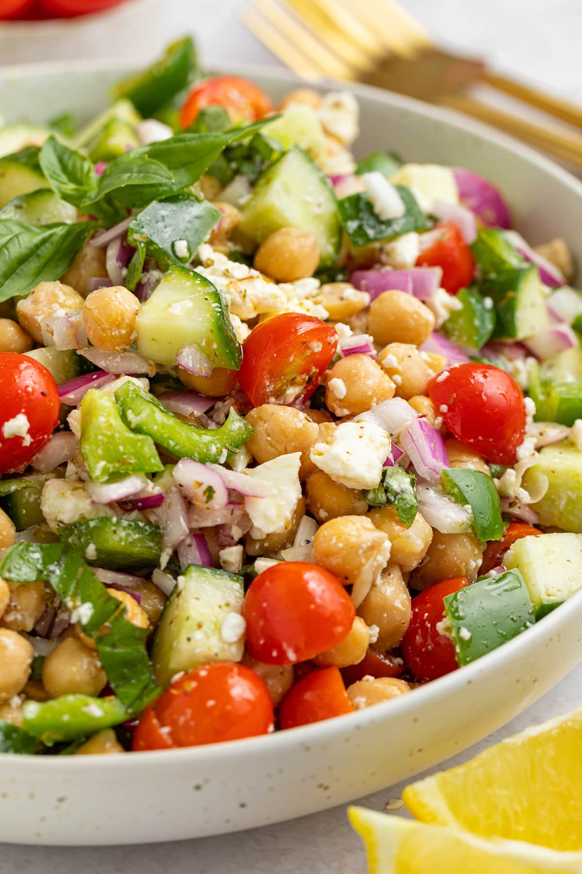 A large white bowl holding a Mediterranean-style chickpea salad with feta, bright red cherry tomatoes, chickpeas, cucumber, onion, and bell pepper.