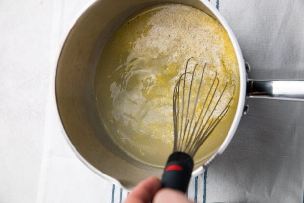 Stirring water and grits in saucepan with whisk
