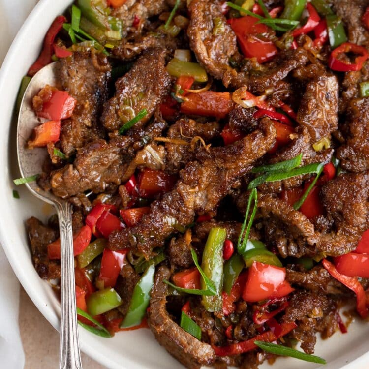 Hunan beef in a white bowl with a silver spoon
