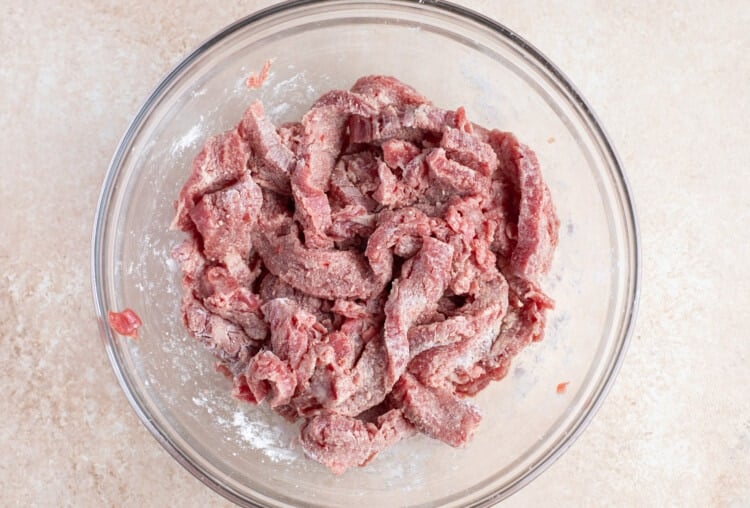Sliced flank steak in a large glass bowl, coated in cornstarch