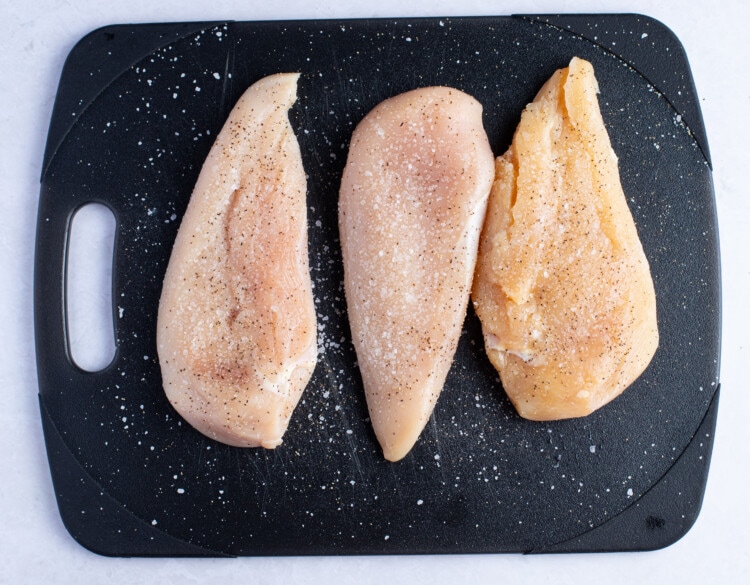 Chicken breasts seasoned with salt and pepper on cutting board