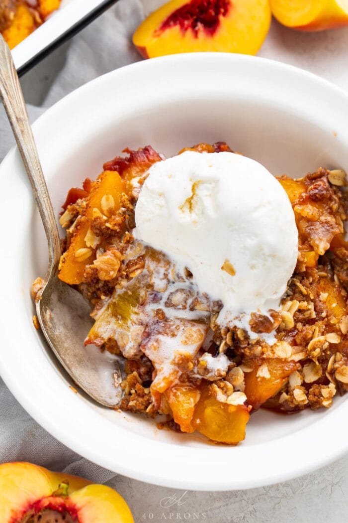 Peach crisp in a bowl topped with vanilla ice cream