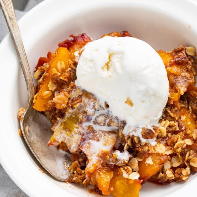 Peach crisp in a bowl topped with vanilla ice cream