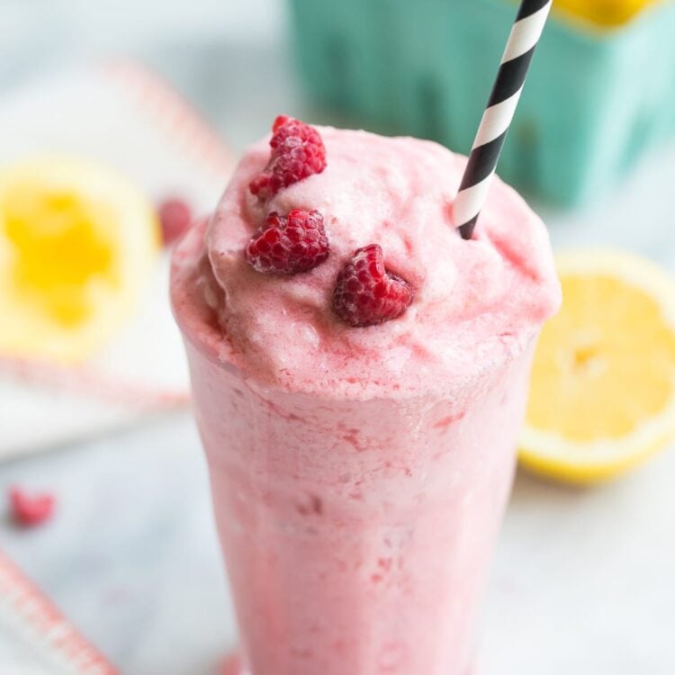 Paleo raspberry frosted lemonade in a glass with a black and white straw and lemons in the background