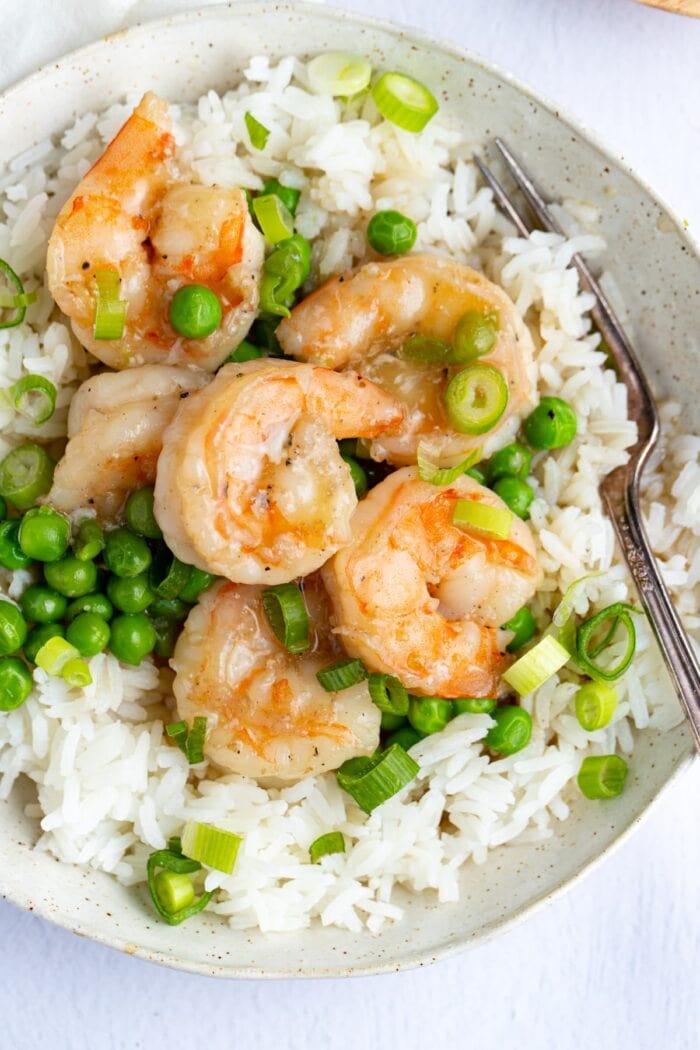 Closeup of shrimp with lobster sauce and peas on a bed of rice in a white bowl