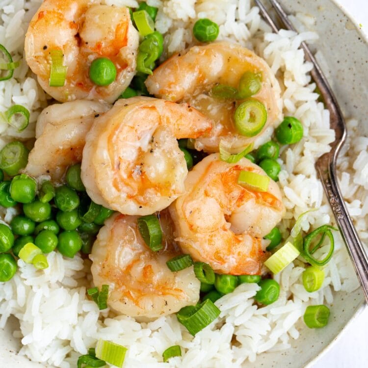 Closeup of shrimp with lobster sauce and peas on a bed of rice in a white bowl