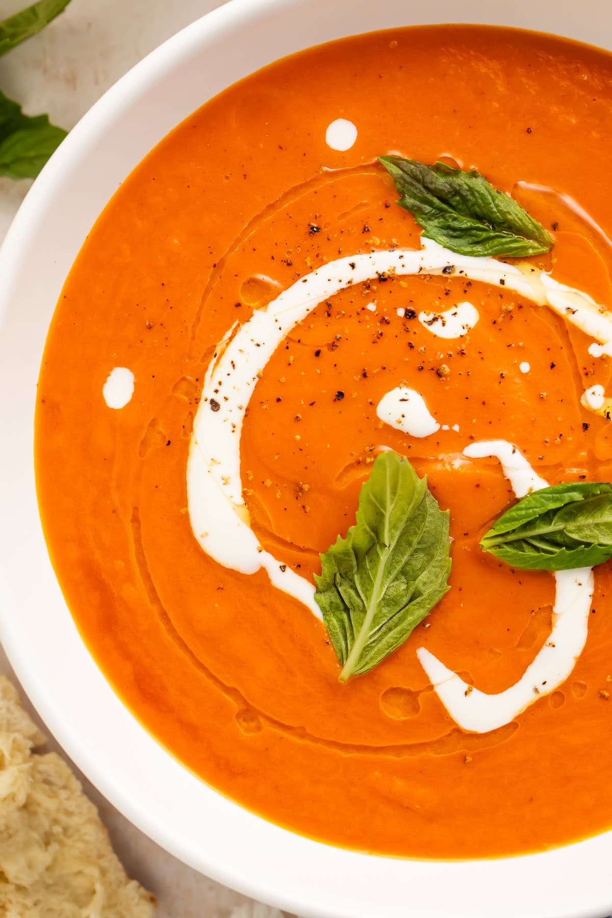 Close-up overhead view of tomato bisque in a white bowl with a cream swirl and fresh basil leaves