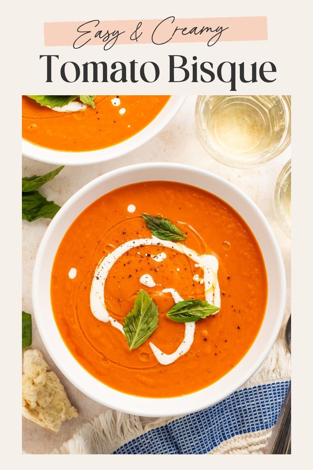 Pinterest pin showing an overhead bowl of creamy tomato bisque with a cream swirl, fresh basil, crusty bread, and a glass of water, with "Easy & Creamy Tomato Bisque" text overlay
