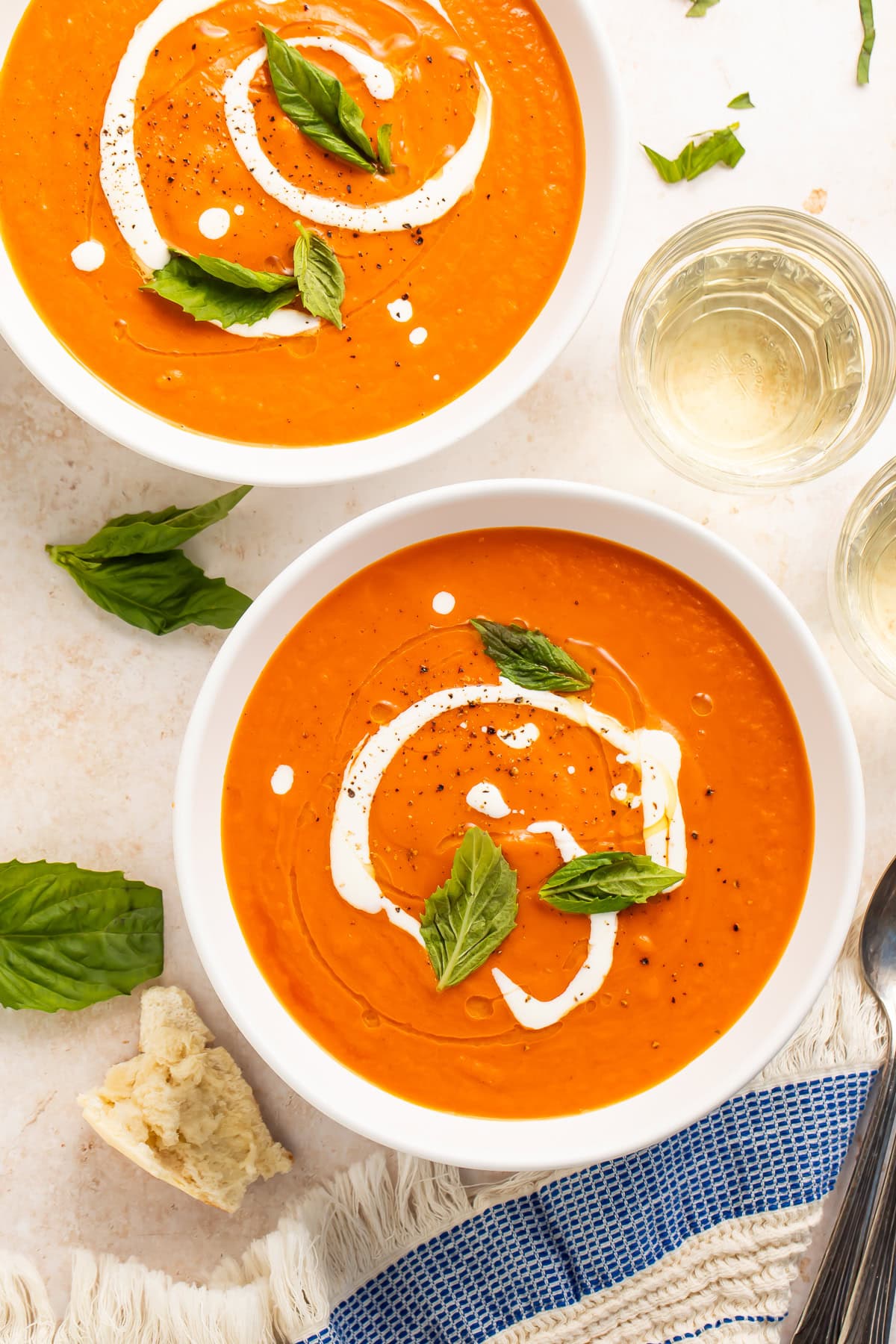 Overhead photo of two bowls of tomato bisque garnished with cream, fresh basil, and cracked black pepper