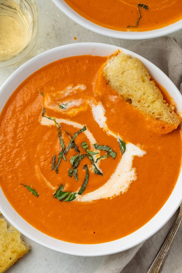 Closeup photo of tomato bisque in a white bowl with a swirl of cream and piece of bread