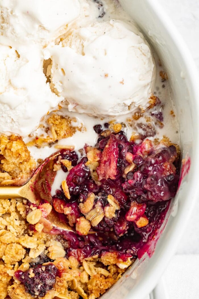 blackberry crumble in a baking dish with a spoon and vanilla ice cream