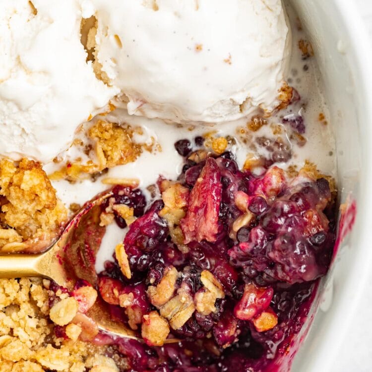 blackberry crumble in a baking dish with a spoon and vanilla ice cream