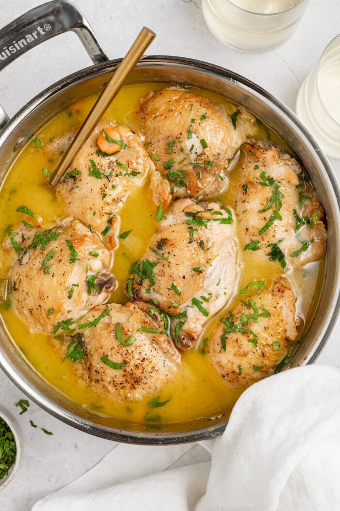 overhead image of chicken fricassee in a skillet with two glasses of white wine and parsley on the side