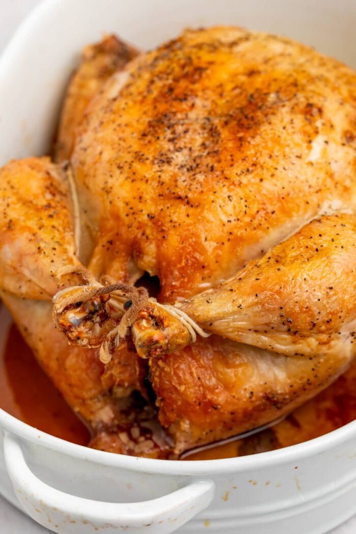 showing how to truss a chicken with a roasted chicken in a baking dish