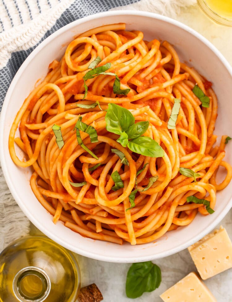 Overhead view of a white bowl of spaghetti swirled with red pomodoro sauce and topped with fresh basil leaves.