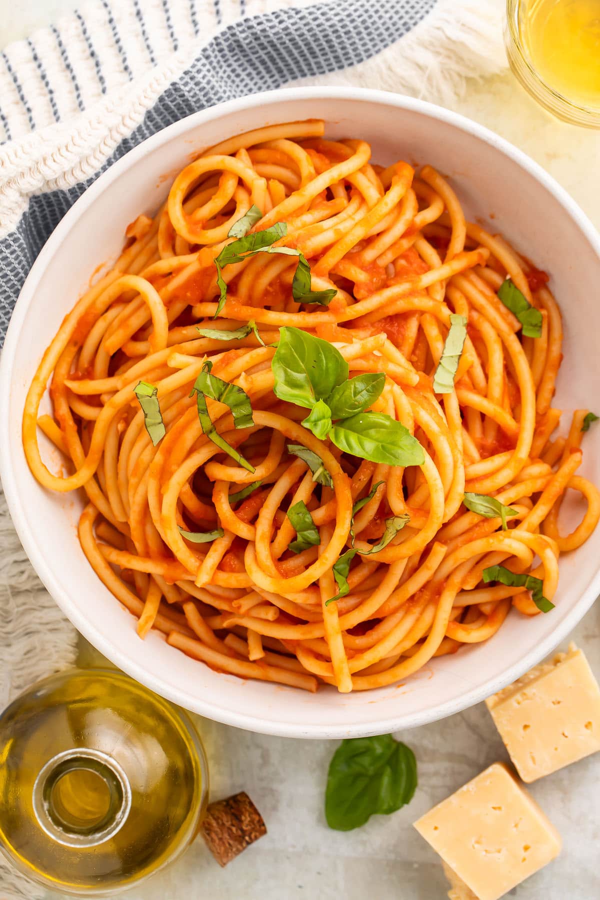 Overhead view of a white bowl of spaghetti swirled with red pomodoro sauce and topped with fresh basil leaves.