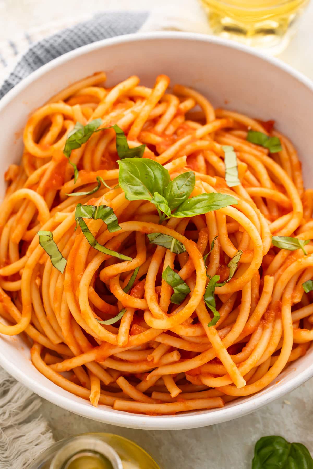 Close-up, overhead view of a white bowl of spaghetti swirled with red pomodoro sauce and topped with fresh basil leaves.