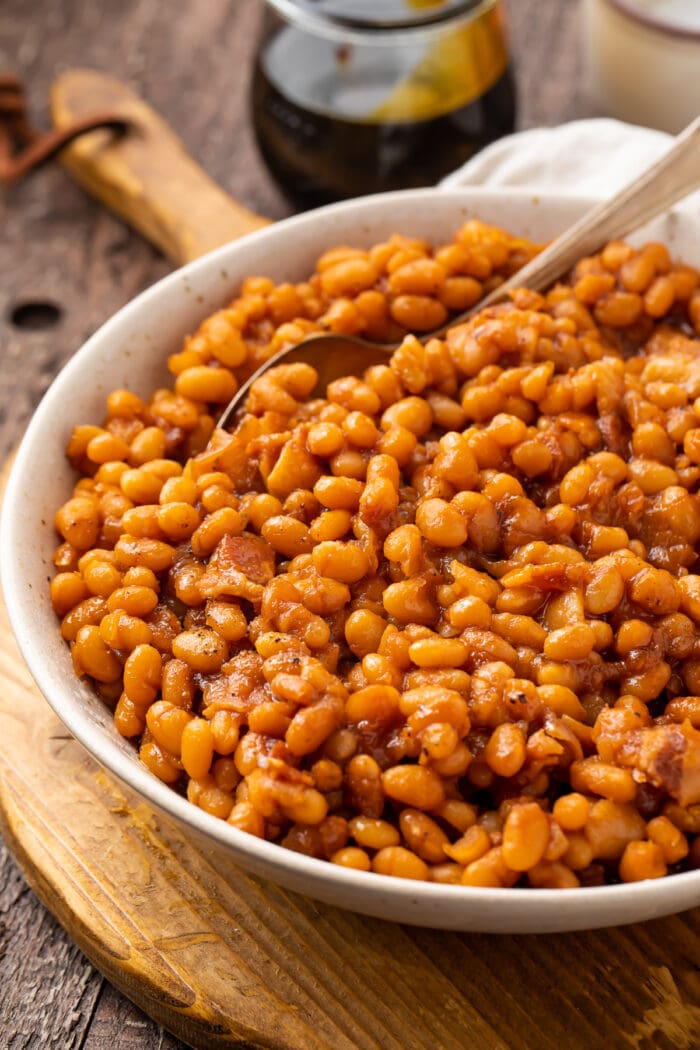 Angled photo of Instant Pot baked beans in a white bowl on a wooden board