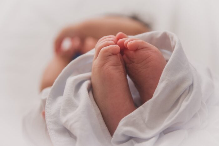 Closeup of baby feet in a blanket with baby's head and arm out of focus in the background - natural birth with epidural