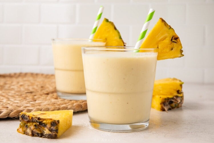 Side view of 2 glasses of pineapple smoothie with pineapple wedges