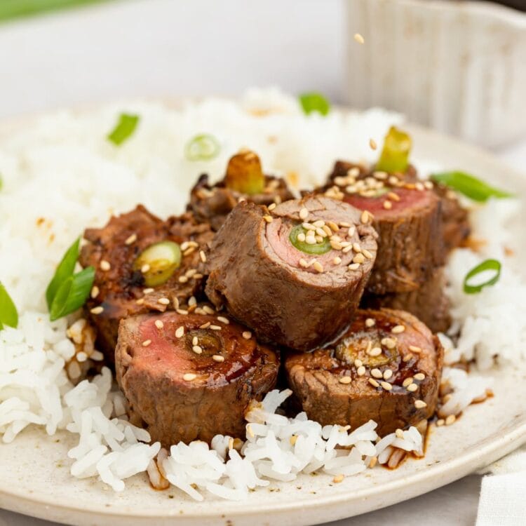 beef negimaki on a plate with rice and sesame seeds being sprinkled over the top