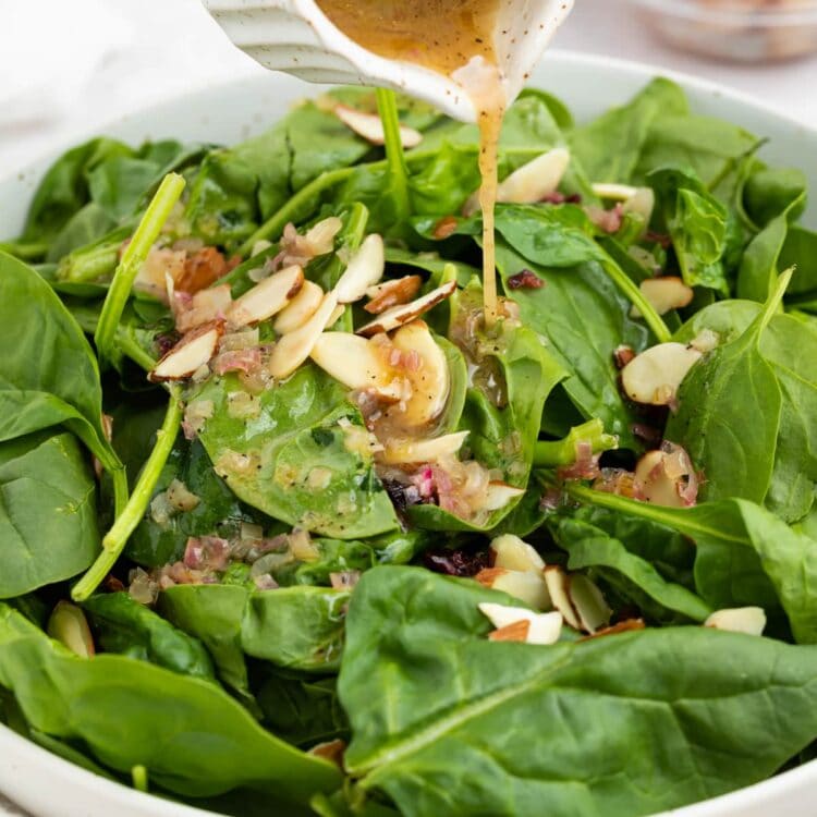 hot bacon dressing being poured over spinach salad